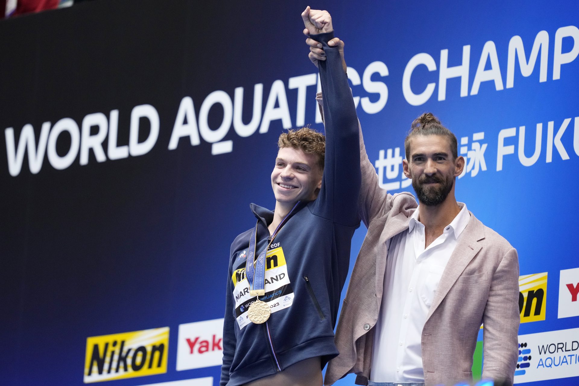 O francês Leon Marchand recebe do ex-nadador americano Michael Phelps a medalha de ouro dos 400m medley da Natação no Mundial de Esportes Aquáticos 2023, em Fukuoka, no Japão - Foto: Eugene Hoshiko/ Associated Press/ Estadão Conteúdo
