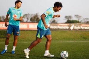 Dois jogadores de uniforme azul e uma bola no campo