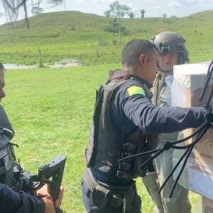 Miliares e funcionários civis do TRE descarregam urnas eletrônicas de um helicóptero em uma área descampada