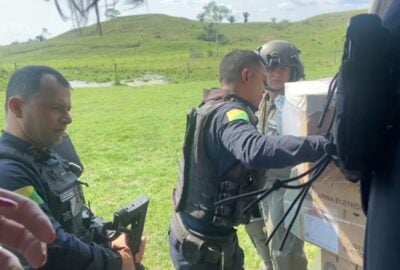 Miliares e funcionários civis do TRE descarregam urnas eletrônicas de um helicóptero em uma área descampada