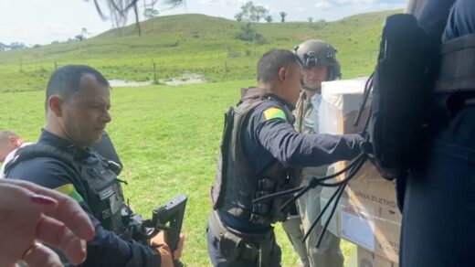 Miliares e funcionários civis do TRE descarregam urnas eletrônicas de um helicóptero em uma área descampada