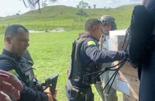 Miliares e funcionários civis do TRE descarregam urnas eletrônicas de um helicóptero em uma área descampada