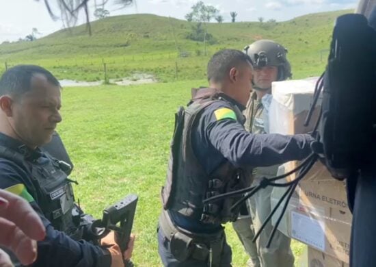 Miliares e funcionários civis do TRE descarregam urnas eletrônicas de um helicóptero em uma área descampada