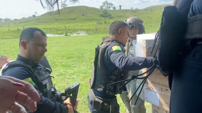 Miliares e funcionários civis do TRE descarregam urnas eletrônicas de um helicóptero em uma área descampada