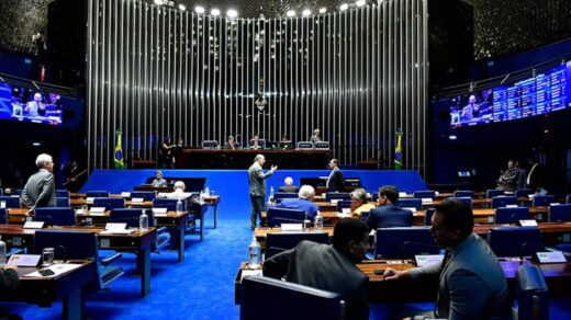 Imagem mostra plenário do Senado Federal, com tapete azul, paredes escuras e alguns senadores