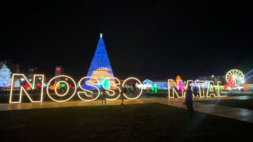 Imagem mostra letreiro iluminado escrito "Nosso Natal" e ao fundo uma árvore de natal gigante, com mais de 30 metros